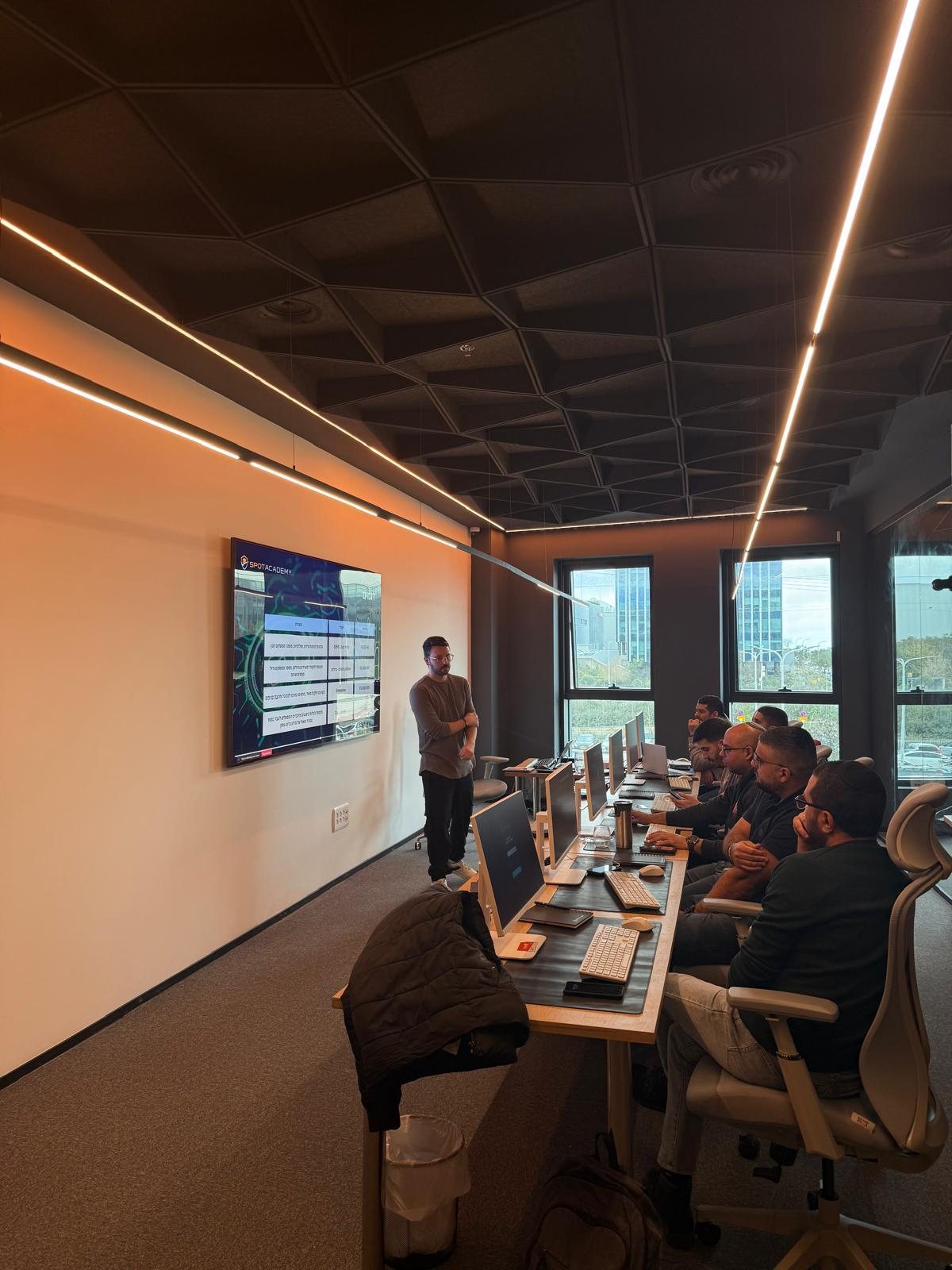 An instructor presenting to a cohort seated at workstations in the SpotAcademy classroom